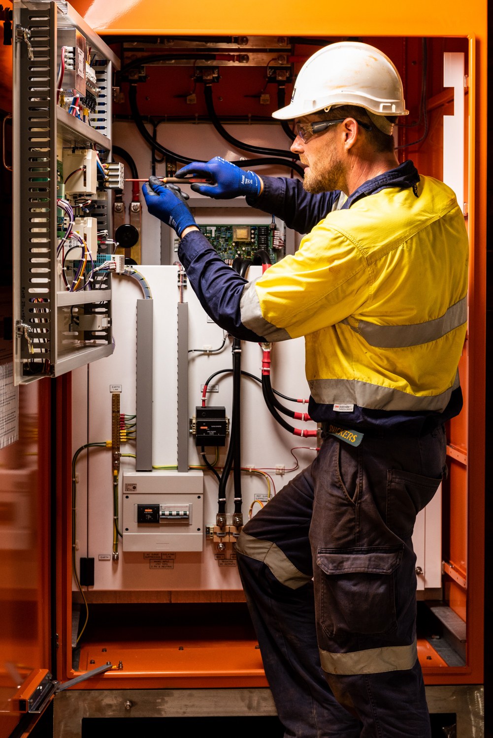 Worker in high-visibility clothing inspecting equipment inside a machinery cabinet