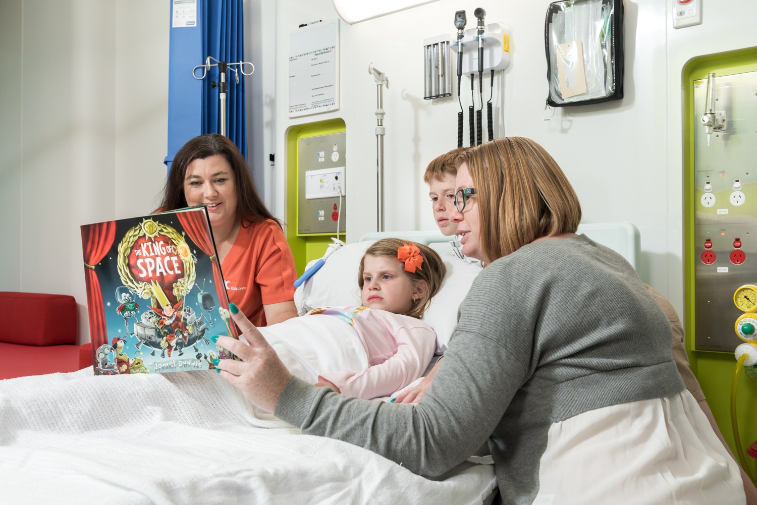 Adults sharing a picture book with a child in a hospital room